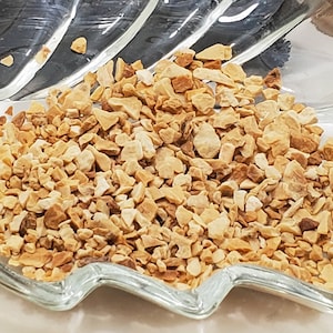 May include: Close-up of a clear, leaf-shaped glass dish filled with small, light brown, irregularly shaped pieces. The dish sits in front of a blurred background. The text "Orris Root" and "7 grams" is visible in the background.
