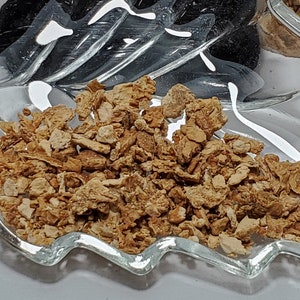 May include: Close-up of a clear glass leaf-shaped dish filled with light brown, irregularly shaped pieces. The dish is on a white surface. In the background, there are other items in a similar dish.
