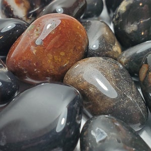 Puede incluir: Una colección de piedras pulidas en varios colores, incluyendo negro, marrón y blanco. Las piedras tienen una superficie lisa y brillante y están pulidas en formas redondeadas. Algunas piedras tienen patrones e inclusiones visibles. Las piedras probablemente se utilizan con fines decorativos o metafísicos.