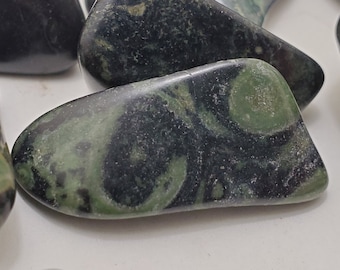 May include: Close-up of several polished stones with a mix of dark green and black colors. The stones have a smooth, rounded shape and a marbled appearance, with swirling patterns of green and black. The stones are likely used for decorative or metaphysical purposes.