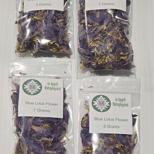Op de afbeelding: Vier doorzichtige plastic zakjes gevuld met gedroogde blauwe lotusbloemen. Elk zakje heeft een wit etiket met de tekst "In Spyrit Metaphysical" en "Blue Lotus Flower". Twee zakjes bevatten 3 gram, en twee bevatten 7 gram.