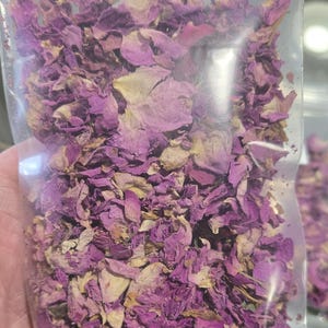 Detailed view of a clear botanical bag filled with dried pink rose petals by InSpyrit Herbs, showcasing a natural mix of fuchsia, soft pink, and magenta floral textures for ritual and decorative use.