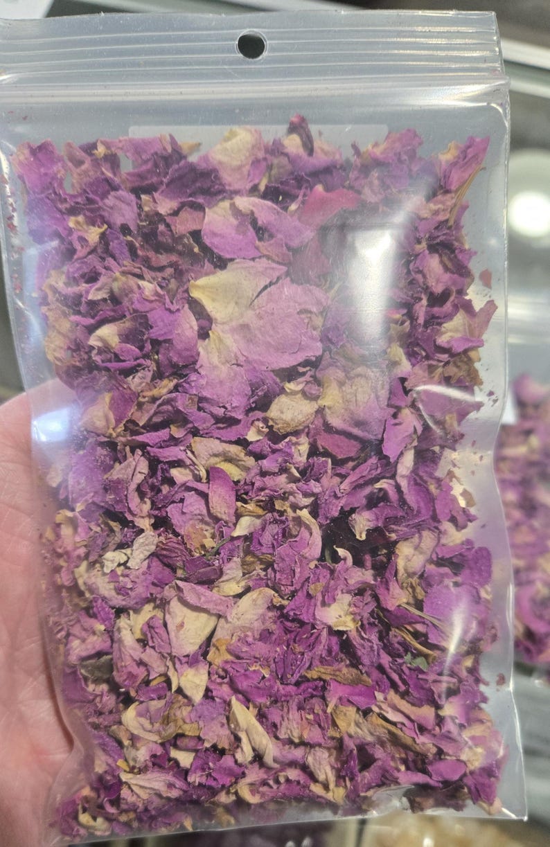 Detailed view of a clear botanical bag filled with dried pink rose petals by InSpyrit Herbs, showcasing a natural mix of fuchsia, soft pink, and magenta floral textures for ritual and decorative use.