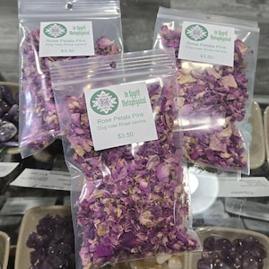 Clear botanical bag filled with dried pink rose petals by InSpyrit Herbs, showing a mix of vibrant fuchsia and soft pink floral textures against a natural background.
