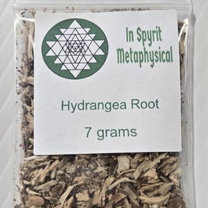 A close-up photograph from InSpyrit Metaphysical showing a single clear plastic bag of dried hydrangea root, with a round white company label marked "Hydrangea Root 7 grams."