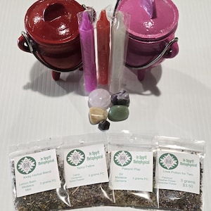 May include: A collection of metaphysical items including two small red and pink cauldrons, candles, crystals, and herbal blends in small bags. The bags are labeled with the text "In Spyrit Metaphysical" and various blend names.