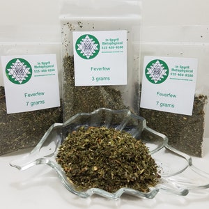 May include: Three clear plastic bags of Feverfew, labeled with the text "In Spyrit Metaphysical" and weights of 3 and 7 grams. A clear glass dish holds a pile of Feverfew. The product is displayed on a white surface.