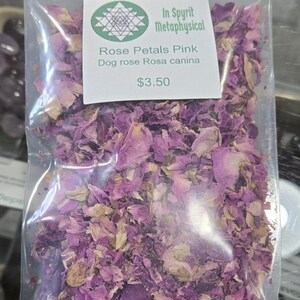 Clear botanical bag filled with dried pink rose petals by InSpyrit Herbs, showing a mix of vibrant fuchsia and soft pink floral textures against a natural background.