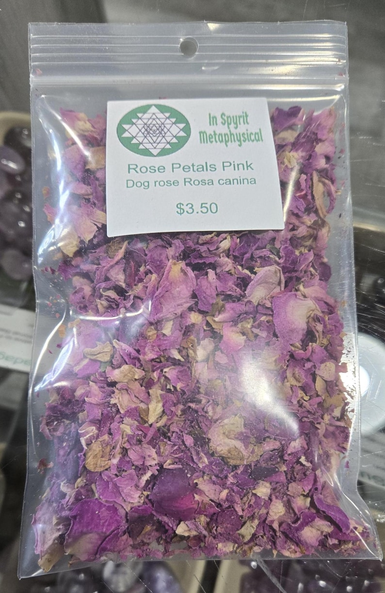 Clear botanical bag filled with dried pink rose petals by InSpyrit Herbs, showing a mix of vibrant fuchsia and soft pink floral textures against a natural background.