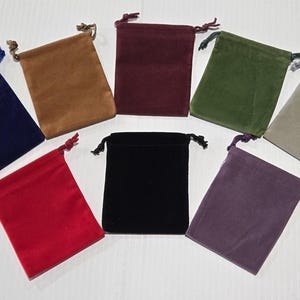 May include: A collection of eight velvet drawstring pouches in various colors, including navy blue, brown, burgundy, green, gray, red, black, and purple. Each pouch has a matching drawstring closure.