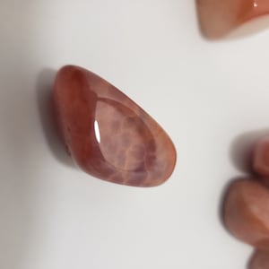 May include: A collection of polished, reddish-brown gemstones with a smooth, glossy surface. The stones have a translucent quality, revealing internal patterns. The lighting creates highlights and shadows, enhancing the stones' natural beauty. The gemstones are likely used for decorative or spiritual purposes.