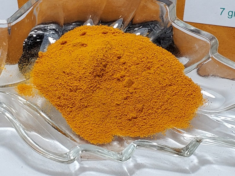 A generous pile of vibrant, golden-yellow Turmeric powder displayed on a decorative leaf-shaped glass dish, highlighting the fine, silky texture and high-vibrancy color of the ground root.