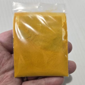 A hand holding a 7 gram bag of InSpyrit Metaphysical Turmeric Powder, showing the volume of the vibrant golden-yellow ground root and the professional branded label.