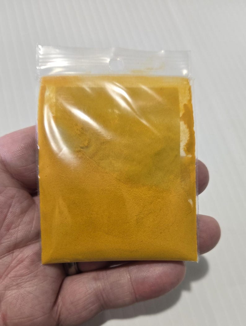 A hand holding a 7 gram bag of InSpyrit Metaphysical Turmeric Powder, showing the volume of the vibrant golden-yellow ground root and the professional branded label.