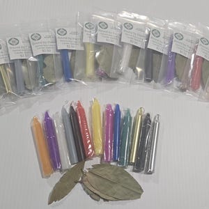 Puede incluir: Una colección de pequeñas velas cónicas multicolores en bolsas de plástico transparentes, cada una acompañada de una hoja de laurel seca. Las velas vienen en varios colores, incluyendo amarillo, azul, morado, blanco, negro y naranja.