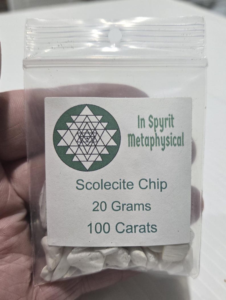 A close-up of a small, clear resealable bag filled with white Scolecite chip stones. The white label is clearly visible with the InSpyrit Metaphysical logo and the text "Scolecite Chip 20 Grams 100 Carats