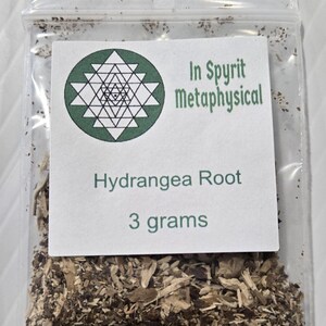 A close-up photograph from InSpyrit Metaphysical showing a single clear plastic bag of dried hydrangea root, labeled with a round white company sticker marked "Hydrangea Root 3 grams."