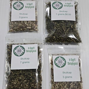ur clear plastic packaging bags filled with dried organic Skullcap Leaf from In Spyrit Metaphysical, laid flat on a white surface. The earthy green botanical blend is visible inside the bags, which feature the shop's logo and are clearly labeled with their 3-gram and 7-gram weights.