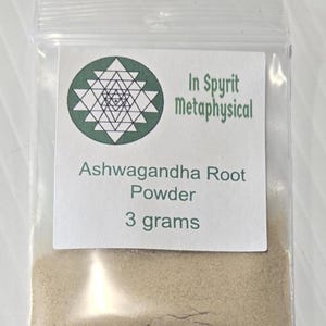 A small, clear bag containing 3 grams of finely ground Ashwagandha Root Powder from InSpyrit Metaphysical. The label features the sacred geometry logo and lists the botanical name Withania Somnifera, showcasing the fine, tan herbal texture.