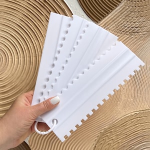 May include: Set of five white plastic cake decorating tools with different scalloped edges. The tools are held in a hand.