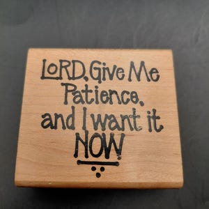 May include: A square wooden block with the words "LORD, Give Me Patience, and I want it NOW" in black lettering. The wood has a light brown color and a visible wood grain. The text is centered on the block.