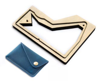 May include: A blue leather card holder with a gold-tone snap button closure and white stitching, accompanied by a wooden cutting die with a black foam outline shaped to create the card holder's pattern, featuring two small metal guide pins.