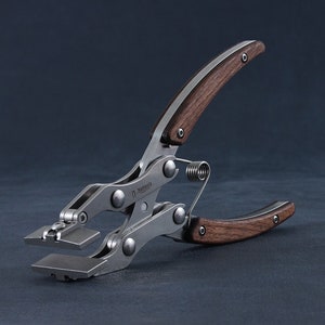 以下が含まれることがあります： 木製のハンドルが付いた金属製のツール。ツールにはバネがあり、2つの平らな長方形のジョーで設計されています。ハンドルは濃い茶色で、金属は銀色です。ツールには「Natools」というテキストがあります。