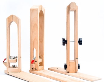 May include: Three wooden leathercraft tools are displayed against a white background. The tools are made of light-colored wood and include adjustable clamps and bases. One tool has a metal clamp with a red lever. The tools are designed for holding leather while sewing.