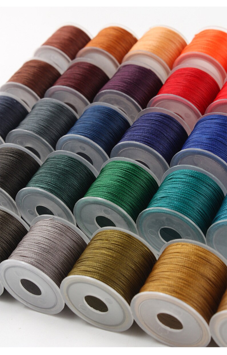 May include: Rows of colorful thread spools in shades of brown, orange, red, blue, green, and gold. The spools are neatly arranged, showcasing a variety of colors for sewing or crafting projects. The thread is tightly wound on clear plastic spools.