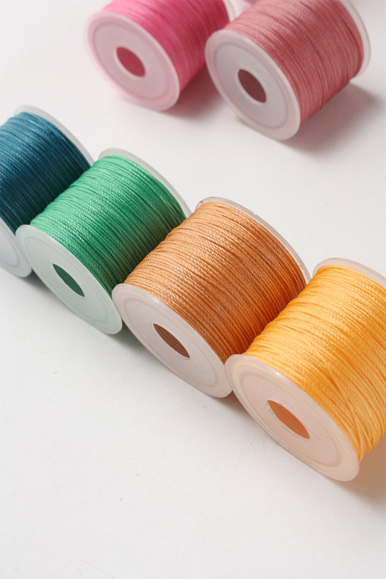 May include: Spools of colorful thread in shades of pink, teal, green, orange, and yellow. The thread is tightly wound on clear plastic spools, ideal for crafting and sewing projects. The spools are arranged diagonally against a white background.