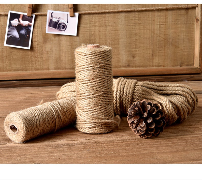 May include: Several spools of natural-colored twine and a length of rope are arranged on a wooden surface. A pine cone sits near the rope. Two small photos are clipped to a wooden background.
