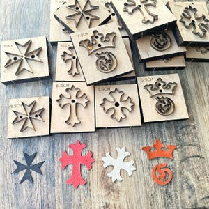 Puede incluir: Troqueles de madera en varias formas, incluyendo cruces, coronas y cruces de Malta. Los troqueles están montados sobre bloques de madera, con tamaños que van de 5,5 cm a 7,9 cm. También hay varias formas de cuero recortadas en rojo, blanco y negro.