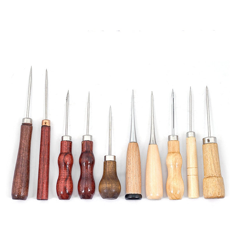May include: A collection of ten awls with wooden handles and metal tips. The handles vary in shape and color, ranging from dark brown to light wood. These tools are designed for piercing and marking materials.