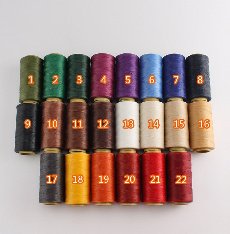 May include: A collection of 22 spools of thread in various colors, numbered 1 through 22. Colors include shades of green, purple, blue, black, brown, white, tan, yellow, orange, and red. The spools are arranged in neat rows.