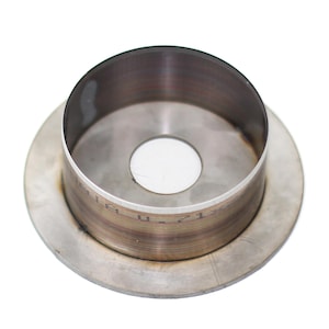May include: A circular metal component with a central aperture and a raised cylindrical edge. The item has a brushed metal finish, likely stainless steel. The rim features etched markings. It rests on a flat, circular base, with a diameter of approximately 10 cm.