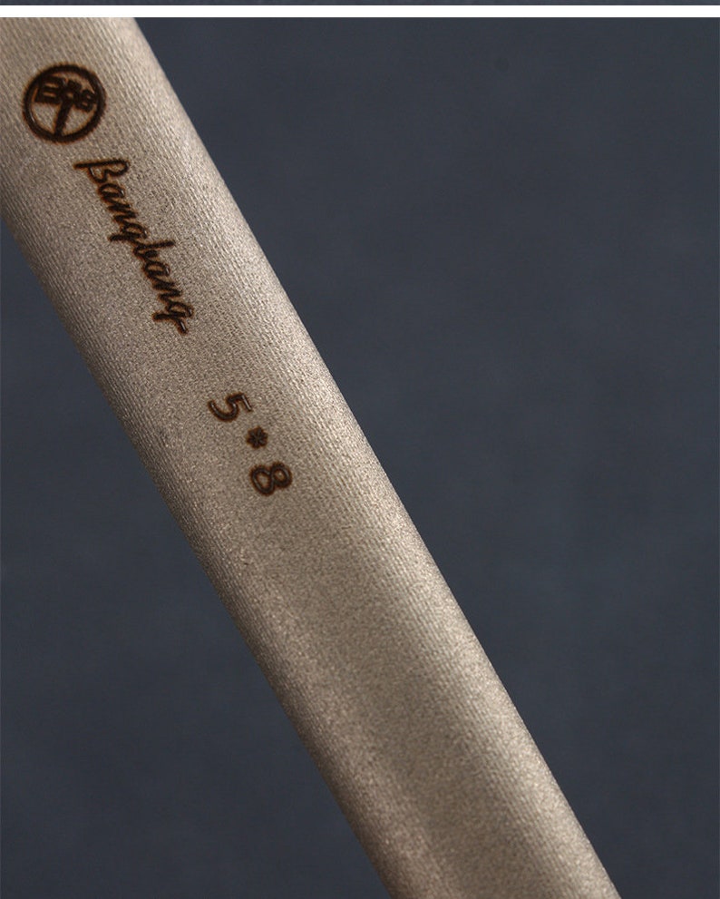 May include: Close-up of a beige cylindrical object with the text "Bangbang 5*8" in a dark brown colour. The object has a textured surface and a logo at the top. The background is a dark grey colour.