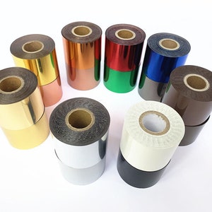 May include: A selection of foil rolls in various colours, including gold, copper, red, green, blue, silver, brown, white, and black. The rolls are arranged in a circle, displaying their shiny surfaces and diverse hues. The rolls are made of a metallic material.