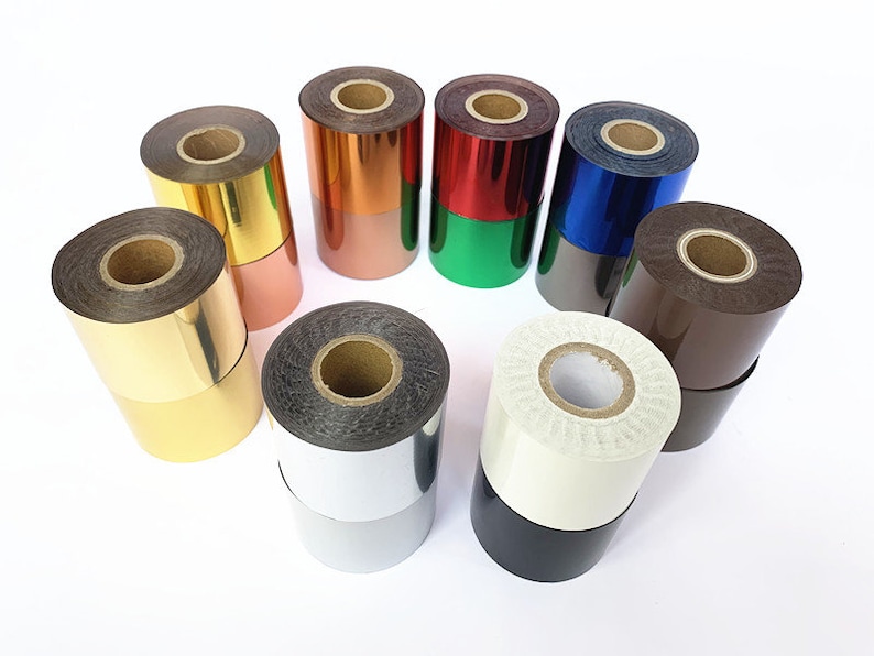 May include: A selection of foil rolls in various colours, including gold, copper, red, green, blue, silver, brown, white, and black. The rolls are arranged in a circle, displaying their shiny surfaces and diverse hues. The rolls are made of a metallic material.