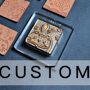 Puede incluir: Una colección de sellos personalizados y etiquetas de cuero repujado. Los sellos son de color dorado y presentan diseños intrincados, incluyendo un abanico y elementos florales. Las etiquetas de cuero son marrones y presentan imágenes en relieve de gatos y caracteres chinos. Se muestra la palabra "CUSTOM".