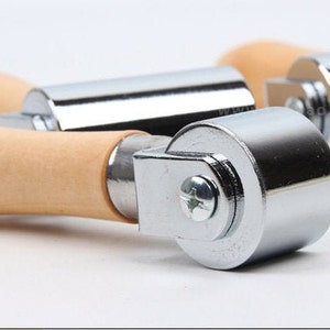 Peut inclure: Gros plan sur trois rouleaux &agrave; main en m&eacute;tal et en bois. Les rouleaux ont un corps cylindrique en m&eacute;tal et une poign&eacute;e en bois. Les parties m&eacute;talliques sont brillantes et r&eacute;fl&eacute;chissantes, et le bois est de couleur brun clair.