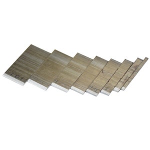 May include: A collection of seven rectangular, silver-colored metal blades, arranged in a slightly angled, descending order. The blades have a matte finish and appear to be new. The edges are sharp and clean. The blades are likely for a utility knife or similar tool.