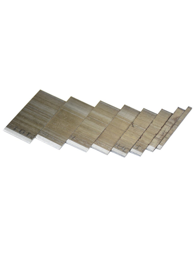 May include: A collection of seven rectangular, silver-colored metal blades, arranged in a slightly angled, descending order. The blades have a matte finish and appear to be new. The edges are sharp and clean. The blades are likely for a utility knife or similar tool.