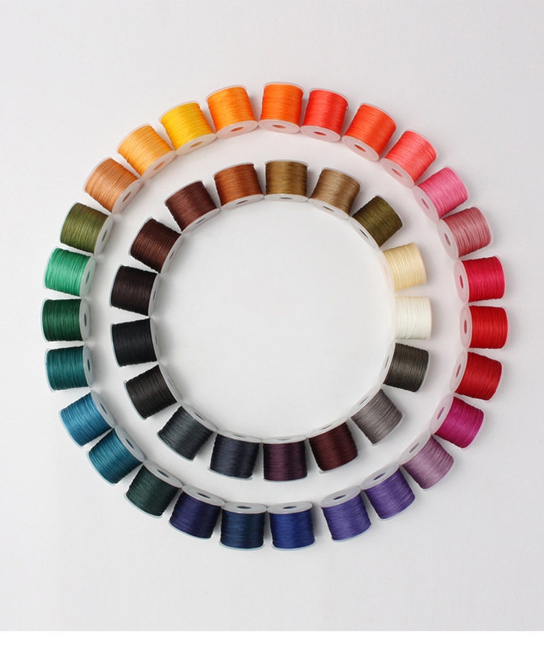 May include: A circular arrangement of colorful thread spools, showcasing a spectrum of hues. The spools are neatly organized, creating a vibrant color wheel. The threads appear to be made of a durable material, suitable for various crafting projects.