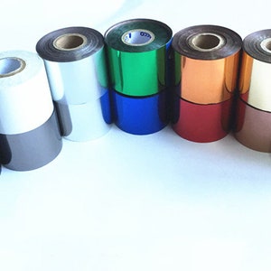May include: An assortment of foil rolls in various colours, including black, silver, white, blue, green, copper, red, and gold. The rolls are stacked, displaying their shiny, reflective surfaces. The image is well-lit, highlighting the range of colours and textures.