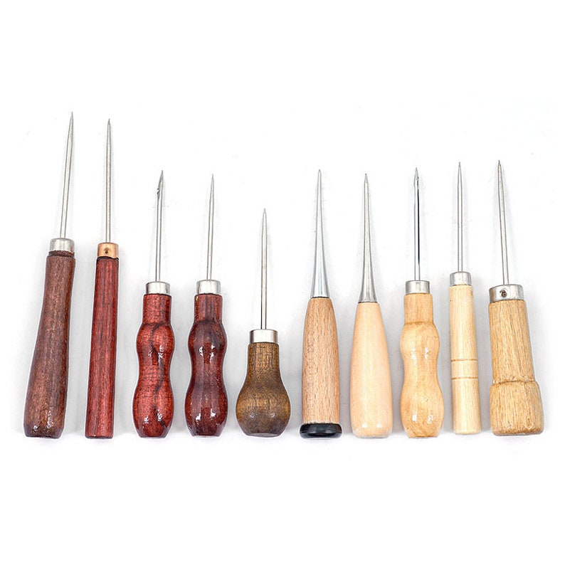May include: A collection of ten awls with wooden handles and metal tips. The handles vary in shape and color, ranging from dark brown to light wood. The awls are arranged in a row against a white background, showcasing their different designs.