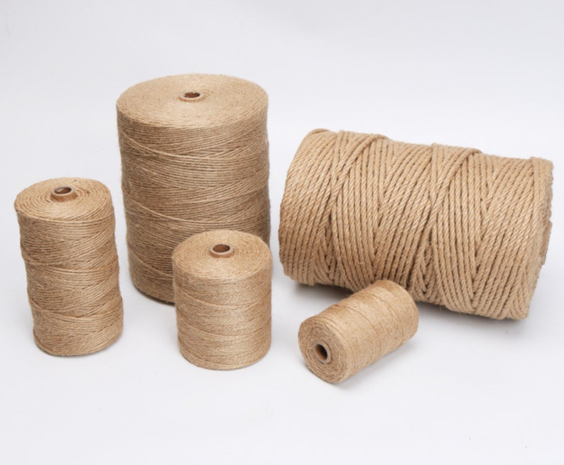 May include: Several spools of natural-colored twine are arranged against a white background. The twine is tightly wound around cardboard cores, with varying sizes and shapes. The twine has a rough, textured appearance, suggesting a natural fiber material.