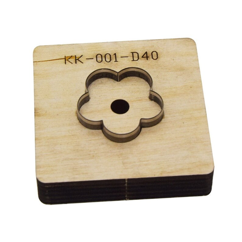 May include: A wooden die-cut tool with a flower shape. The die-cut has a square base with a flower-shaped cutout in the center. The text "KK-001-D40" is printed on the top surface. The tool is made of light brown wood.