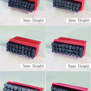 Puede incluir: Un juego de sellos de letras en una caja roja, con alturas que var&iacute;an de 3 mm a 10 mm. Los sellos negros est&aacute;n dispuestos en filas, con el texto "Set of letters" en la parte superior.