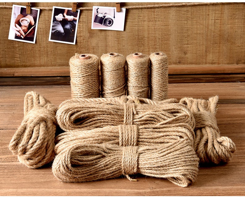 May include: Several spools of natural jute twine and bundles of rope are arranged on a wooden surface. Three small photos are clipped to a string in the background. The twine and rope are a light brown color.