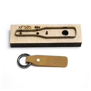 May include: A wooden die-cut tool with the text "XF505" and a metal keychain. The die-cut tool is in the shape of a bottle opener. The keychain is made of tan leather and has a silver metal ring.